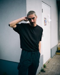 a man in a black t - shirt leaning against a wall